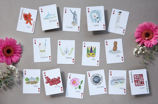 Alabama-themed playing card deck featuring watercolor illustrations of state landmarks, cities, and symbols including the USS Alabama, Yellowhammer, and cotton fields