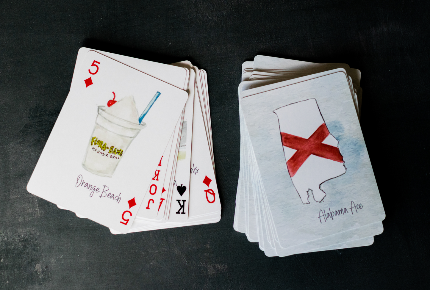 Alabama-themed playing card deck featuring watercolor illustrations of state landmarks, cities, and symbols including the USS Alabama, Yellowhammer, and cotton fields