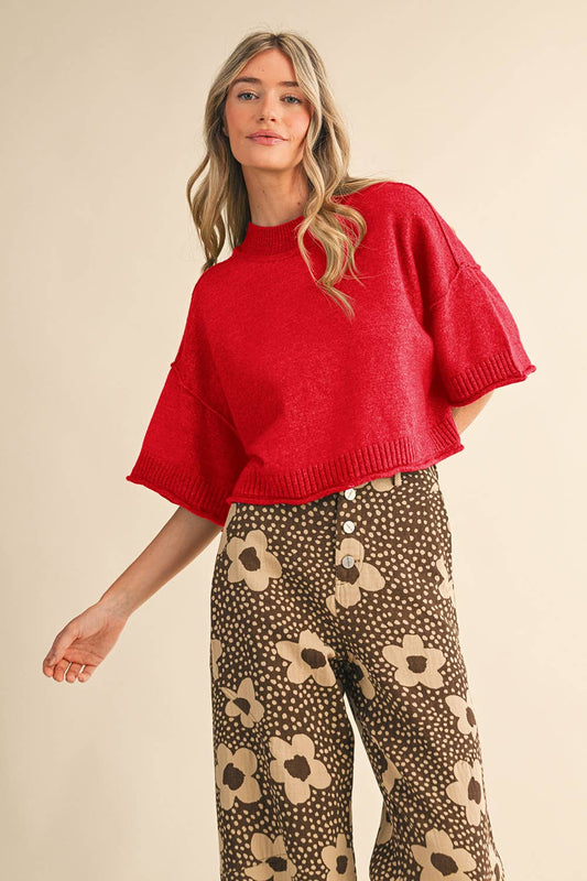 Woman wearing a red sweater and patterned pants on a beige background